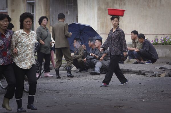 Uma mulher norte-coreana equilibra um balde na cabeça, enquanto homens fumam na rua no final de um dia de trabalho, na quarta-feira, 22 de junho de 2016, em Wonsan, Coreia do Norte. - Sputnik Brasil