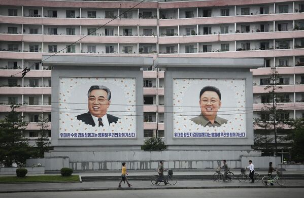 Norte-coreanos parecem anões face aos retratos gigantes dos líderes norte-coreanos Kim Il-sung e Kim Jong Il num prédio de apartamentos, na quarta-feira, 22 de junho de 2016, em Wonsan, Coreia do Norte. - Sputnik Brasil