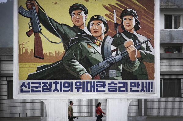 Um homem e uma mulher norte-coreanos caminham sob um mural com uma mensagem que diz: “Viva a grande vitória da política ‘Exército em primeiro lugar’!” no centro da cidade de Wonsan, na quarta-feira, 22 de junho de 2016, em Wonsan, Coreia do Norte. - Sputnik Brasil