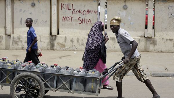 Um jovem passa por uma rua da cidade nigeriana de Kano transportando água, em 8 de abril de 2016; a inscrição na parede diz: Mate Boko Haram e não xiitas - Sputnik Brasil