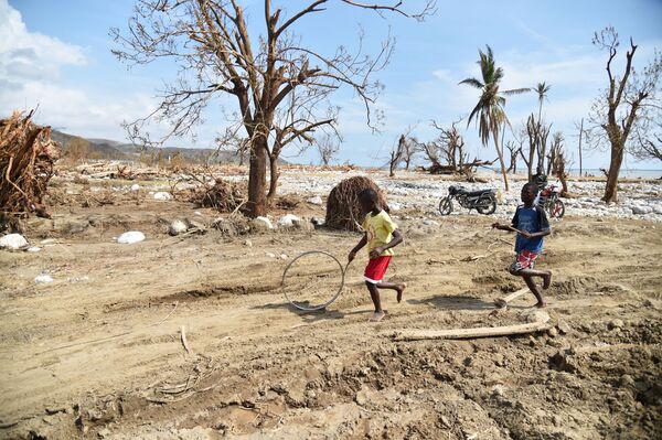 Meninos empurram um pneu entre as ruínas da cidade de Les Cayes (Haiti), afetada pelo furacão Matthew - Sputnik Brasil
