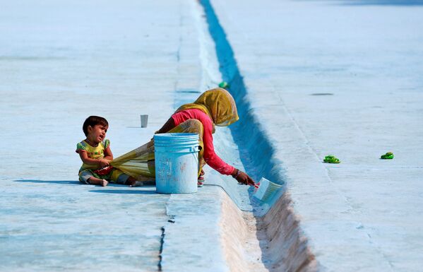 Uma mulher pinta um aqueduto enquanto sua filha tenta chamar sua atenção em Deli, Índia - Sputnik Brasil