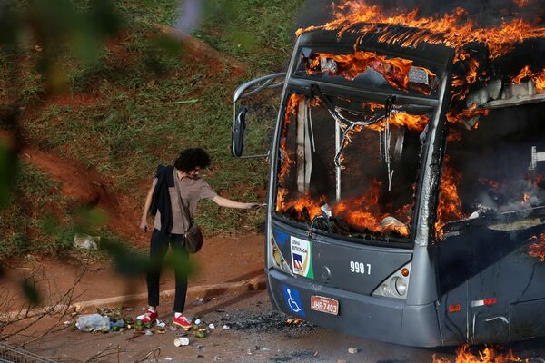 Homem acende cigarro no ônibus em fogo durante manifestações antigovernamentais em Brasília - Sputnik Brasil
