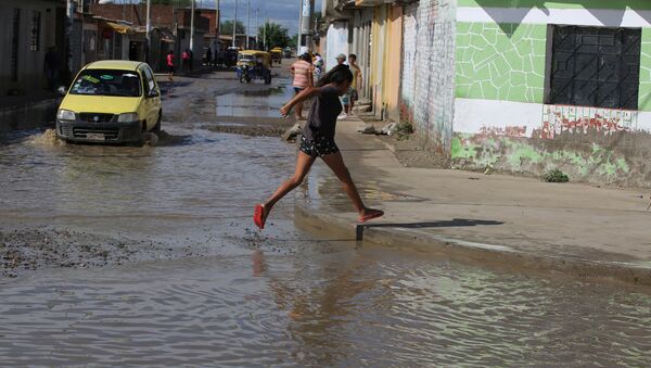 A woman cross a flooded street damaged after heavy rain in El Indio district of Piura, northern Peru - Sputnik Brasil