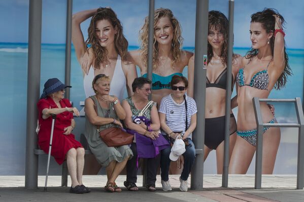 Mulheres aguardam por um ônibus na parada de transporte público com publicidade de roupas de praia, em Madri - Sputnik Brasil