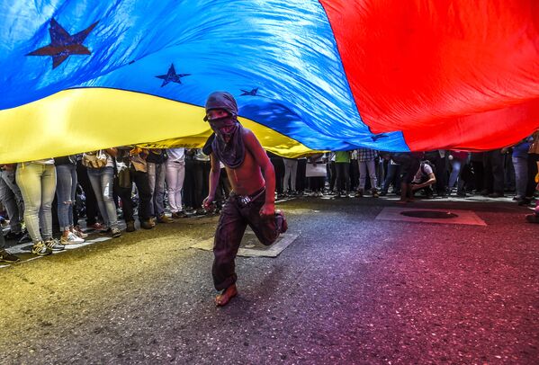 Menino corre sob a bandeira venezuelana durante protestos de jornalistas e funcionários da mídia em Caracas - Sputnik Brasil
