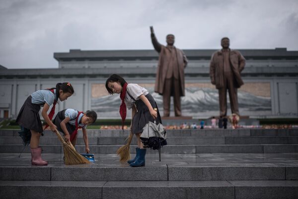 Crianças limpam os degraus perto dos monumentos de Kim Jong-il e Kim Il-sung na Coreia do Norte, no âmbito dos festejos do Dia da Vitória - Sputnik Brasil