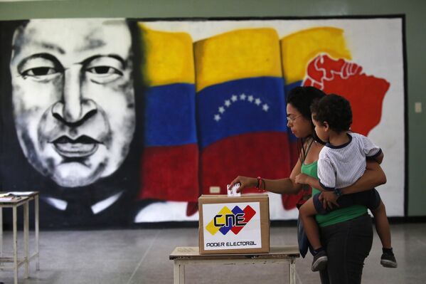 Mulher vota em frente a mural de Hugo Chávez, em Caracas. - Sputnik Brasil