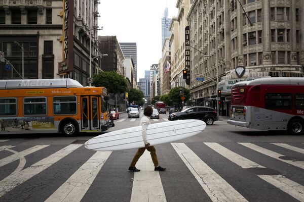 Homem atravessa uma rua no centro da cidade americana de Los Angeles segurando prancha de surfe - Sputnik Brasil