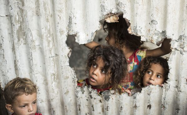Crianças palestinas olham através de um buraco no cercado em um bairro pobre de Gaza - Sputnik Brasil