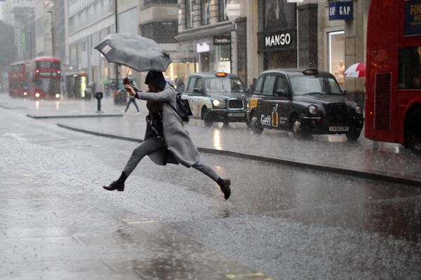 Uma pedestre pula para atravessar a rua durante um aguaceiro em Londres - Sputnik Brasil