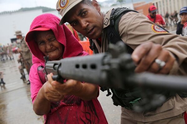 Policial das Forças Armadas venezuelanas ensina mulher como usar fuzil durante exercícios militares em Caracas - Sputnik Brasil